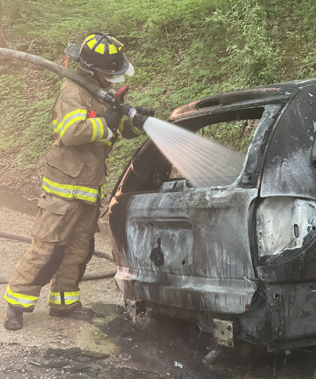 Fireman spraying a hose in a burnt vehicle