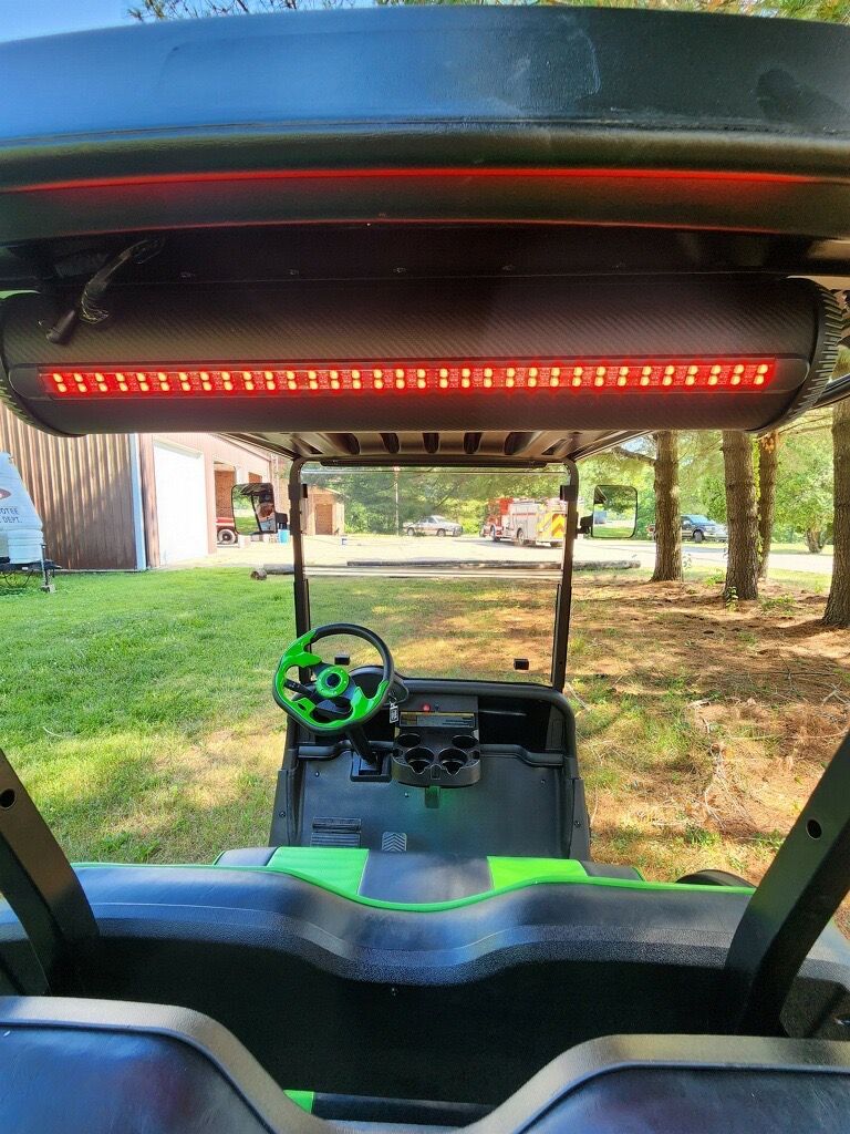 A golf cart with a green steering wheel is parked in a grassy field.
