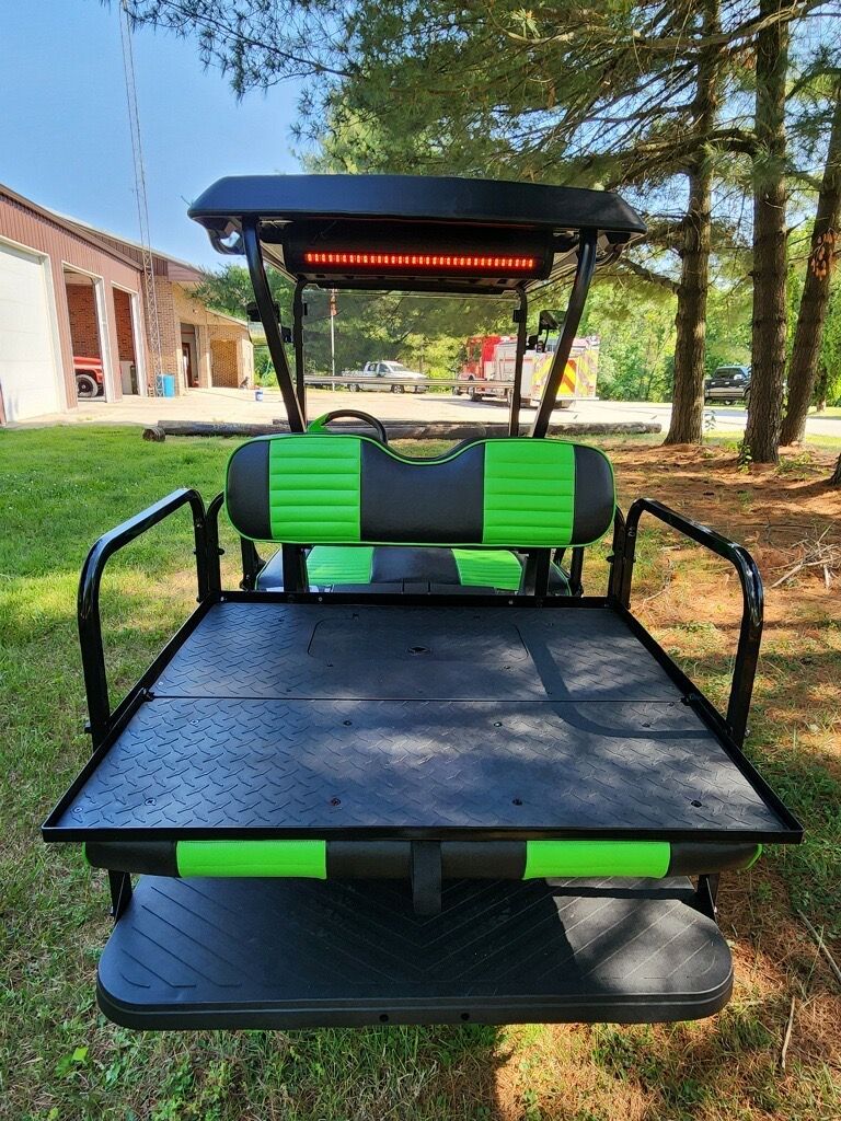 A black and green golf cart is parked in the grass.
