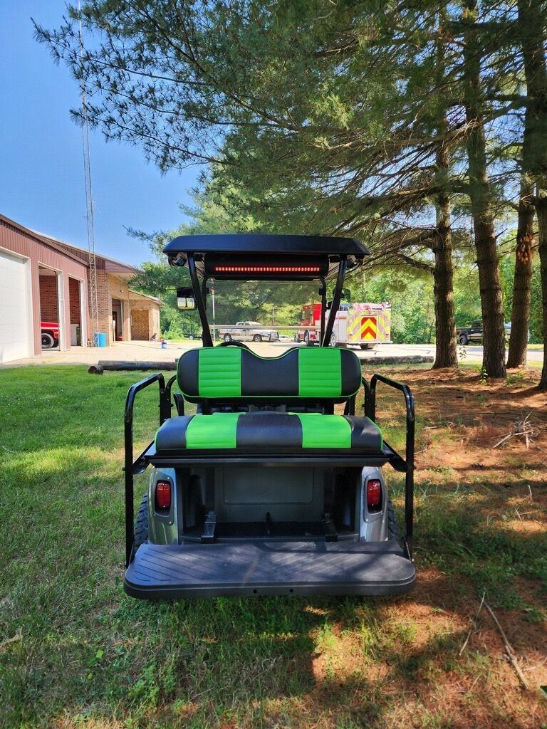A black and green golf cart is parked in a grassy field.