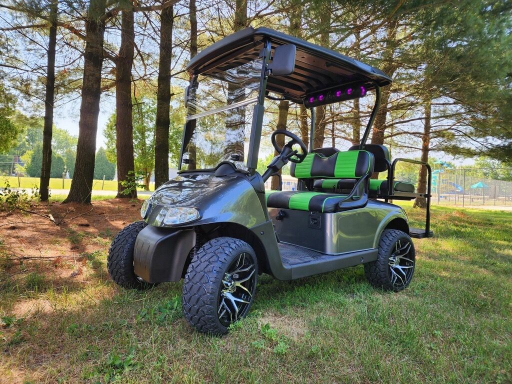 A golf cart is parked in the grass in front of a forest.