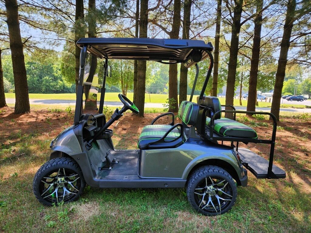 A golf cart is parked in the grass in the middle of a forest.
