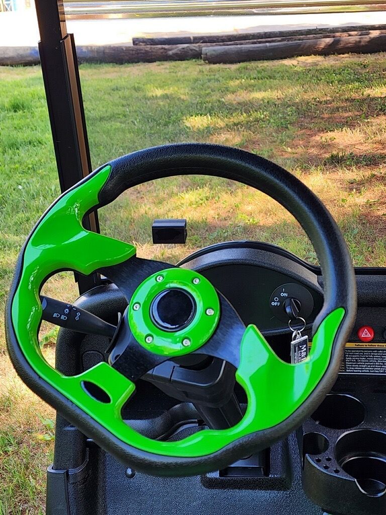 A green and black steering wheel on a golf cart.