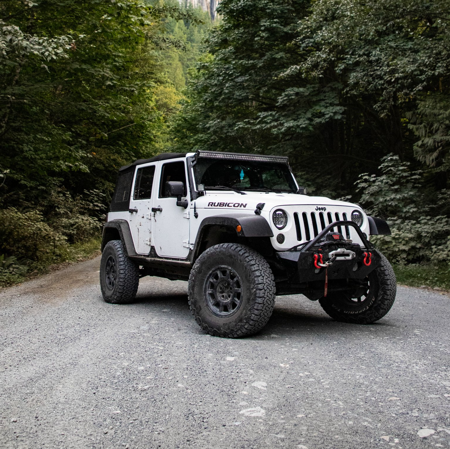 A white jeep is parked on a gravel road in the woods.