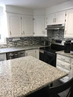 A kitchen with granite counter tops , stainless steel appliances , and white cabinets.