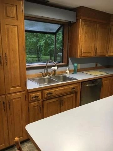 A kitchen with wooden cabinets , a sink , a dishwasher and a window.