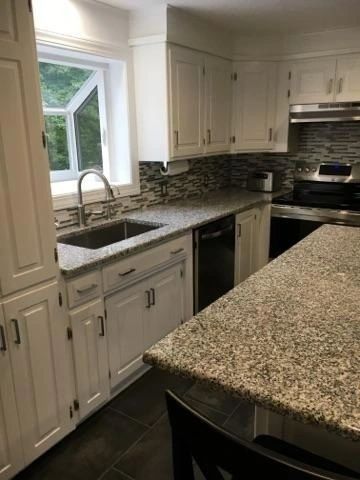 A kitchen with granite counter tops , white cabinets , a sink , and a stove.