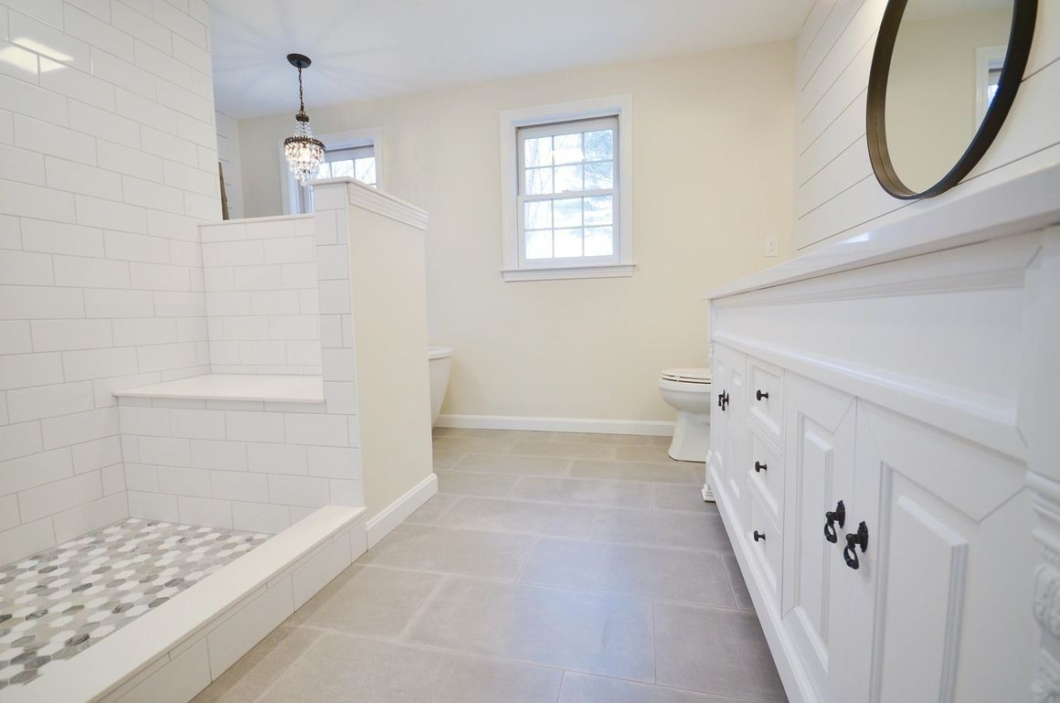 A bathroom with white cabinets , a toilet , and a walk in shower.