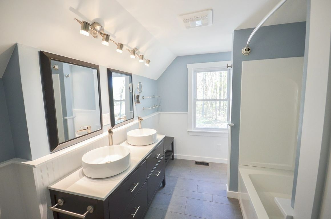 A bathroom with two sinks , two mirrors and a tub.