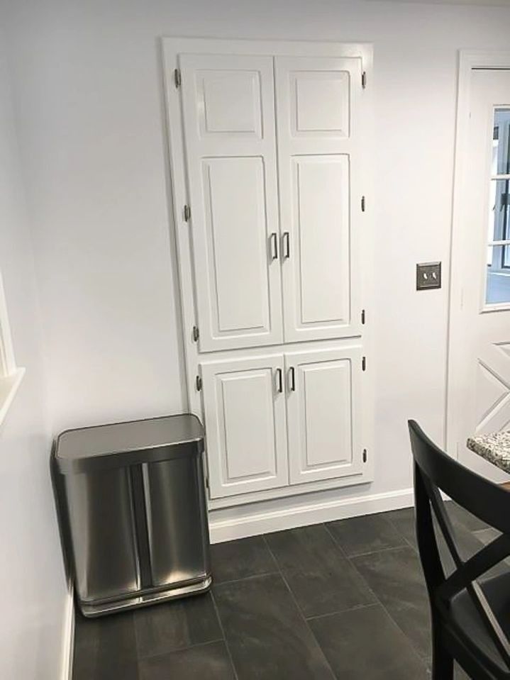 A kitchen with white cabinets and a stainless steel trash can.
