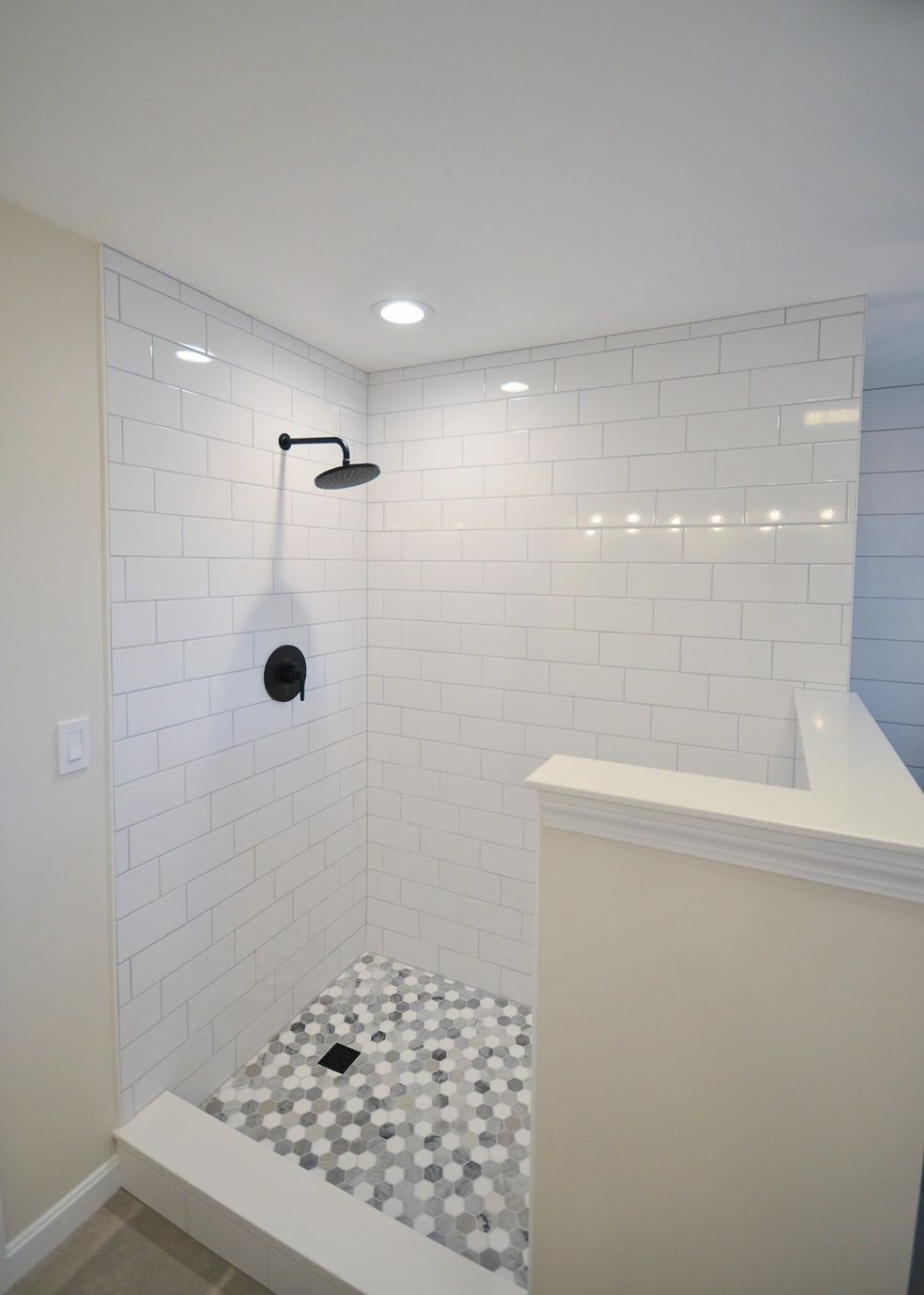 A shower with white tiles and a black shower head.