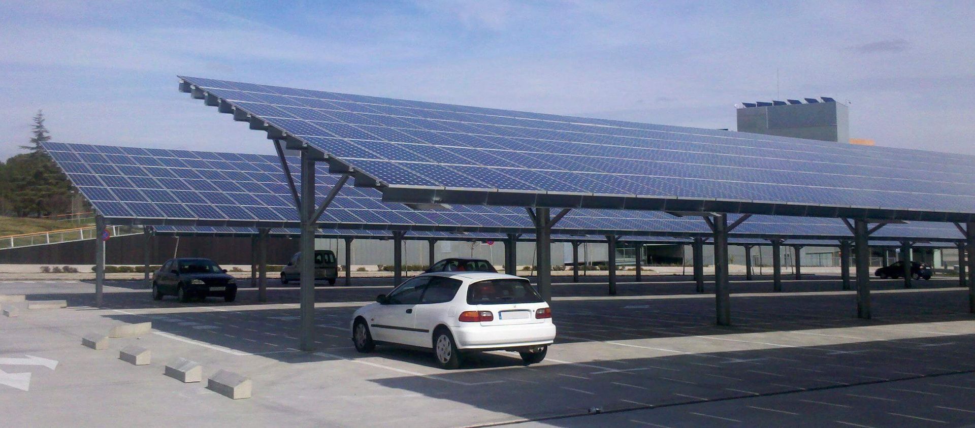 A white car is parked under a canopy of solar panels.