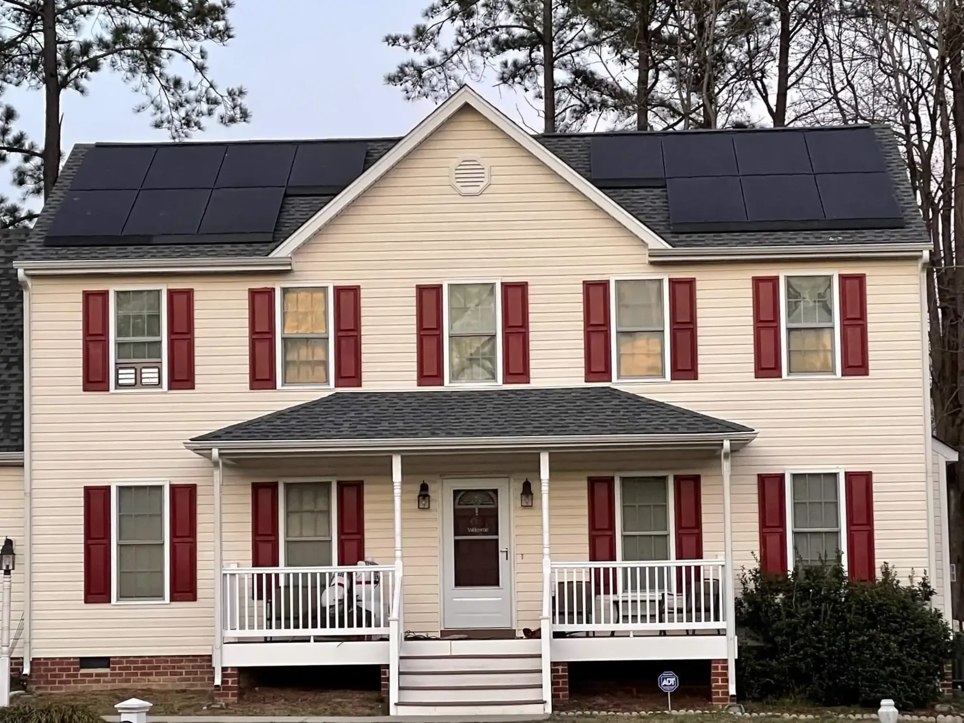 A large white house with red shutters and solar panels on the roof.