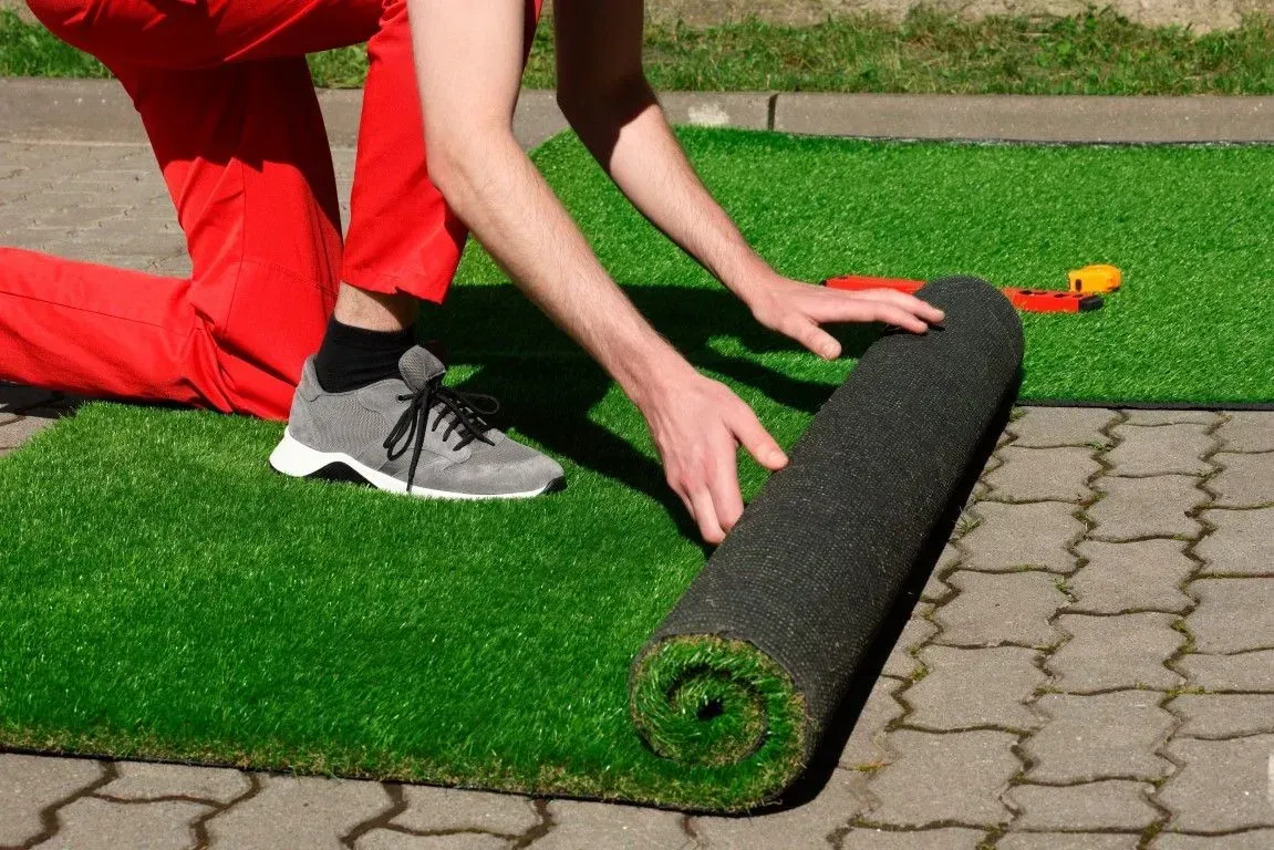 Person installing a roll of artificial turf on a stone patio.