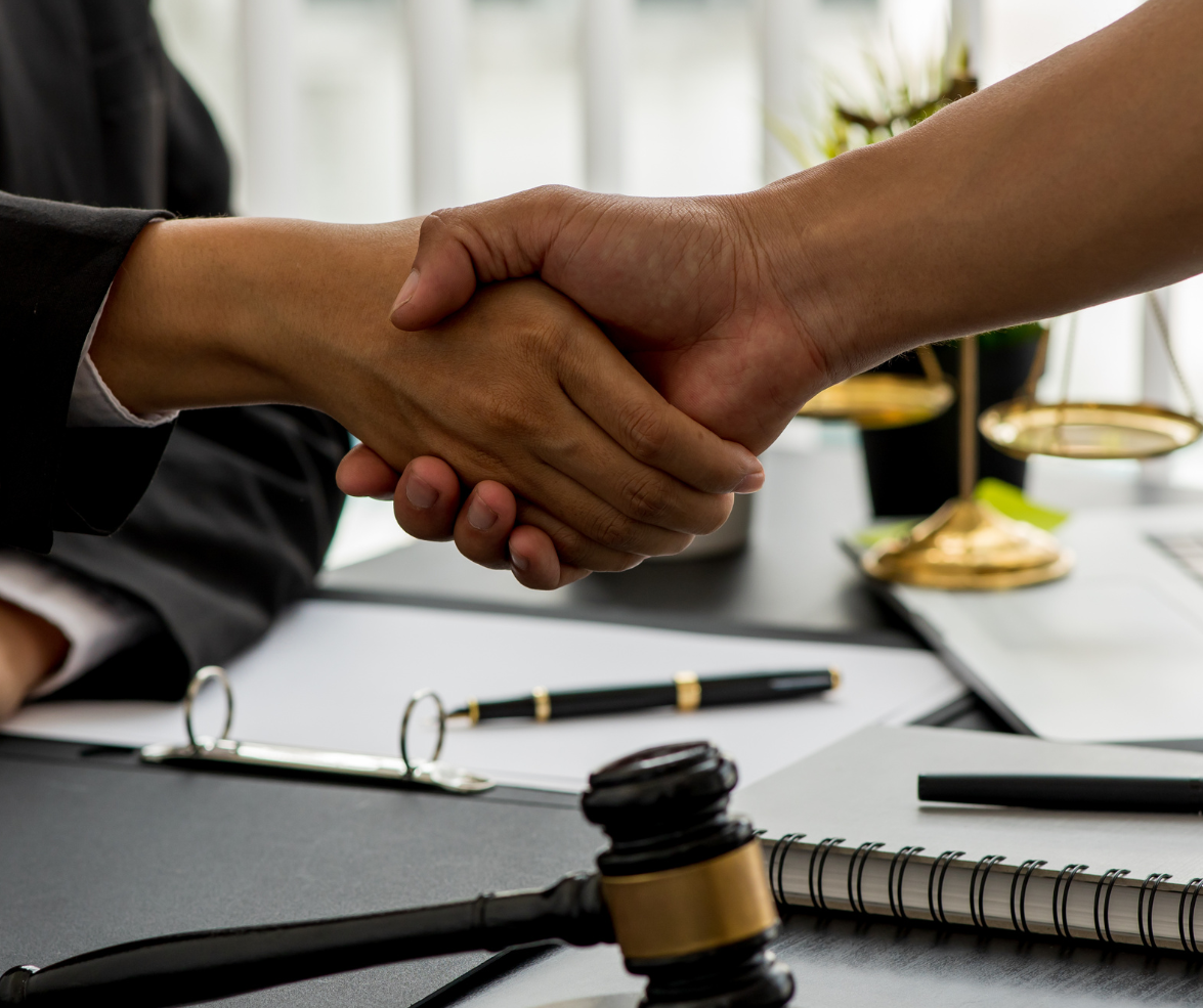 Hands shaking over a desk with a gavel and scales of justice, likely after a legal agreement.