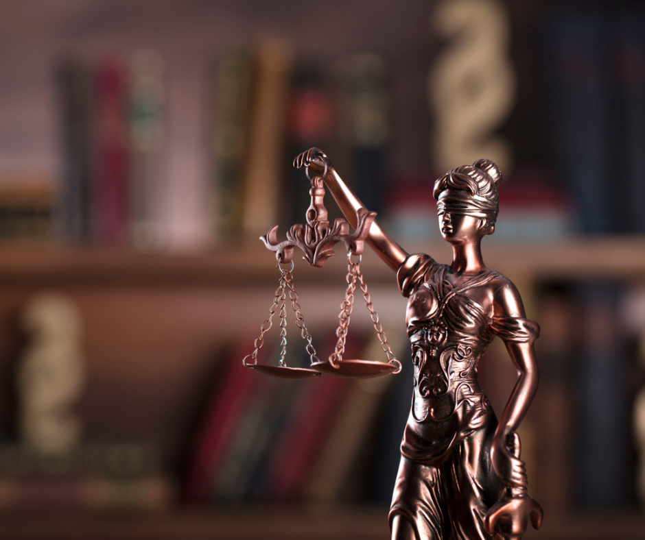 Bronze Lady Justice statue holding scales with bookshelf in background