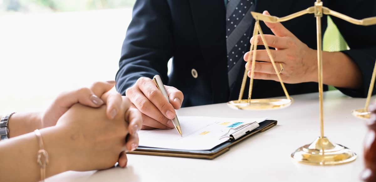 Hands signing a document at a desk with a gold scales of justice nearby