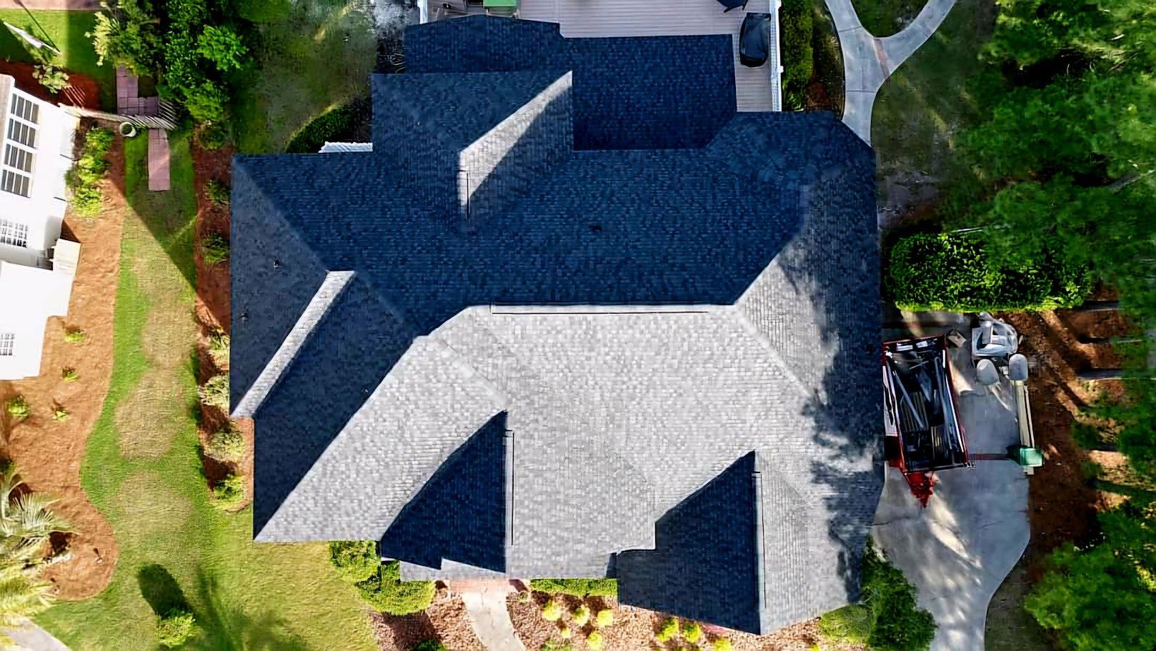 Overhead view of a dark blue shingled roof with multiple sections on a house with a green lawn.