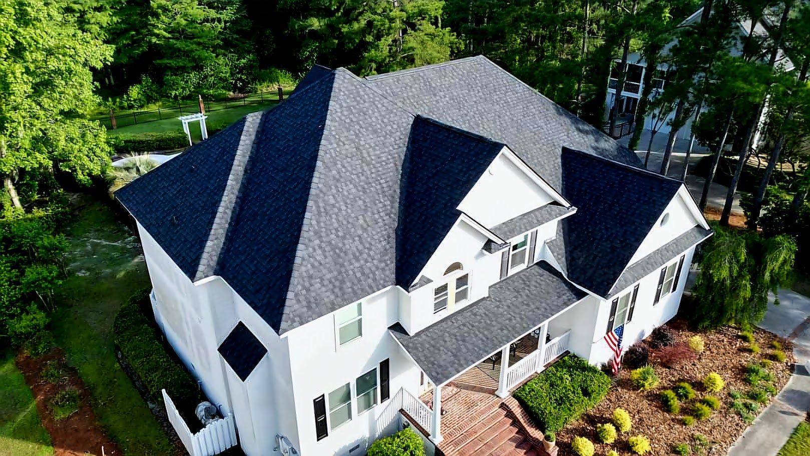 White house with a dark gray roof surrounded by green trees and grass.