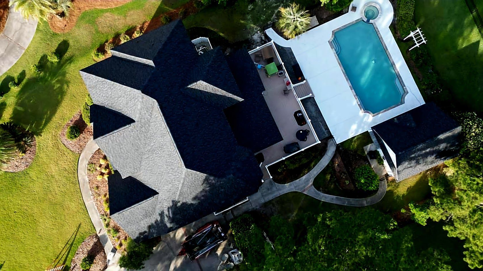 Aerial view of a dark roof house with a rectangular pool and green lawn.