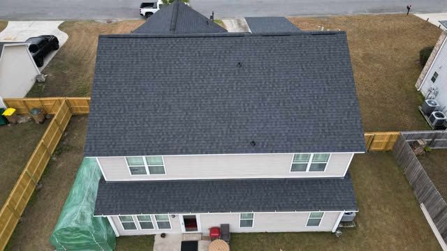 Overhead view of a two-story house with a dark gray shingled roof, surrounded by a wooden fence and lawn.