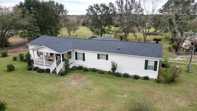 White mobile home with dark roof, green shutters, porch.