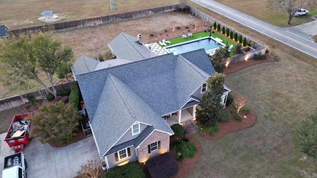 Aerial view of a large house with a pool in the backyard, driveway, and landscaping.