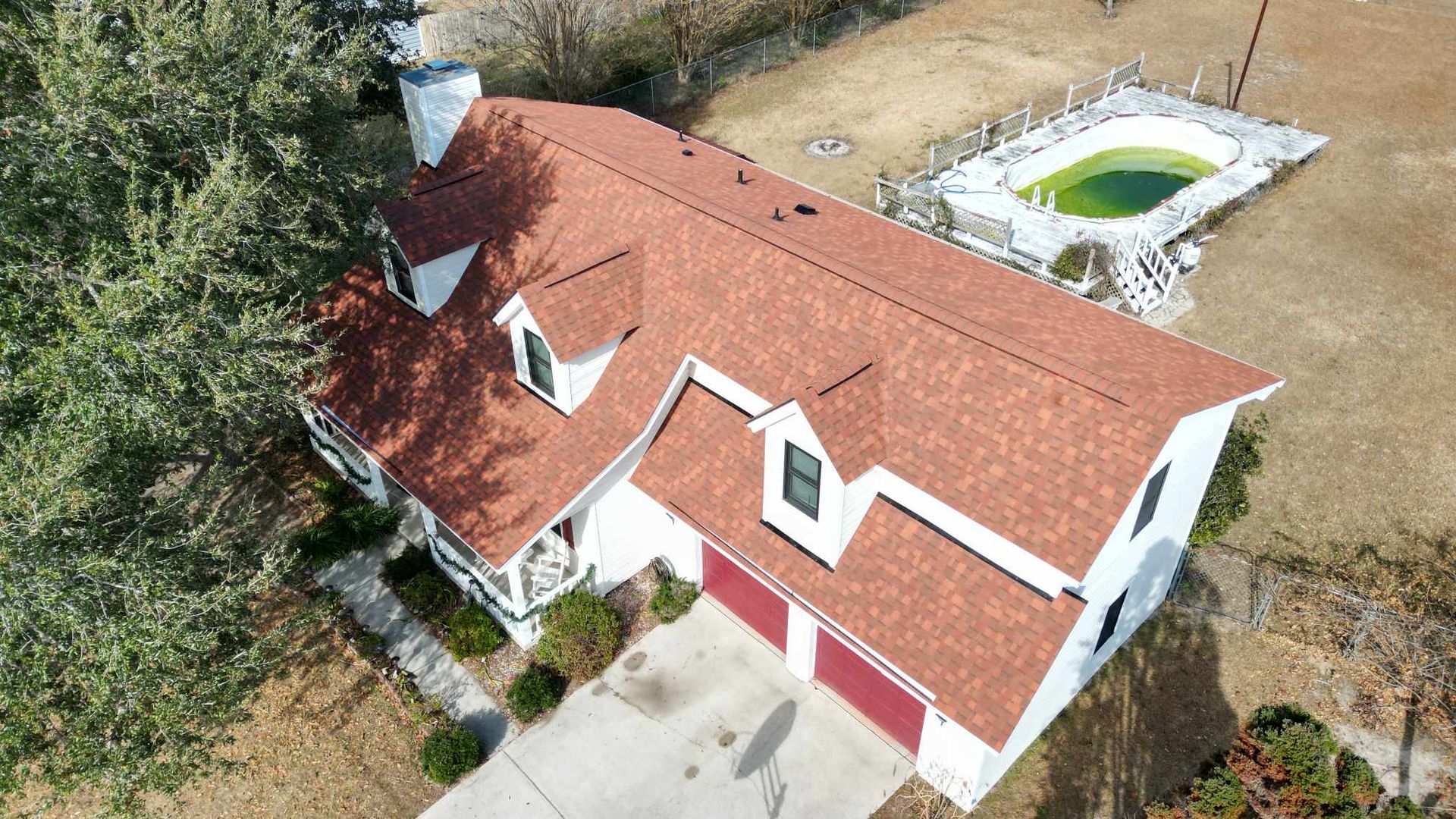 Aerial view of a white house with a red roof, a driveway, and a backyard with a pool.