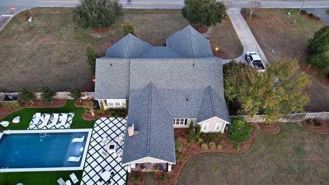 Aerial view of a house with pool, yard, and driveway. Gray roof, blue pool, white lounge chairs.