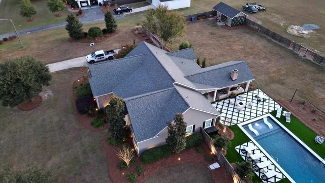 Aerial view of a house with a pool in a yard. Grey roof, beige exterior, green lawn.