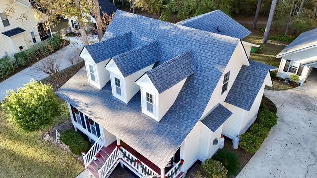 Overhead view of a house with a blue shingled roof, multiple dormers, and white siding.