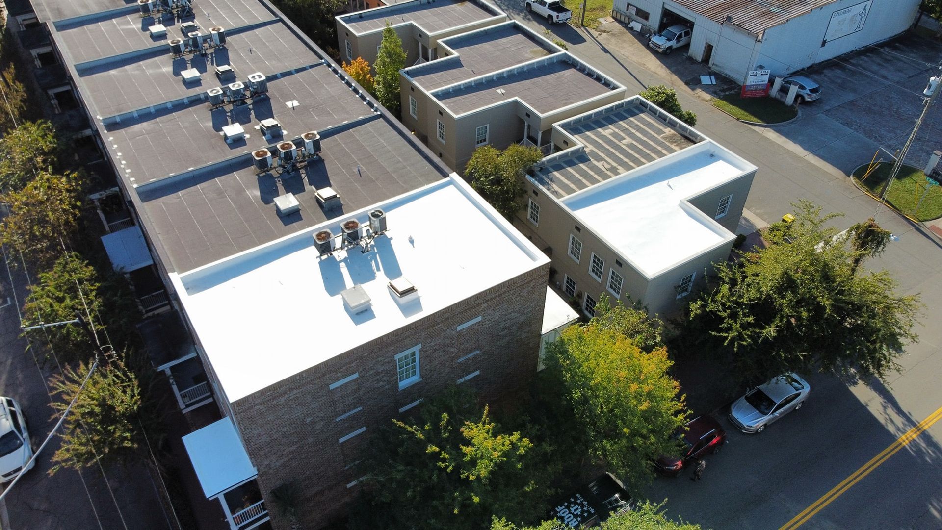 Aerial view of apartment buildings with flat roofs and parked cars on street.