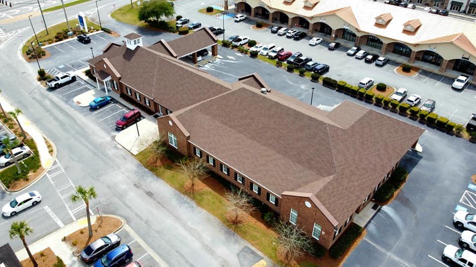 Aerial view of a long, brown-roofed building with surrounding parking lots and street.