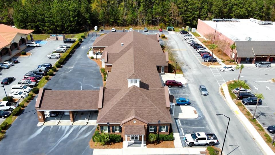 Aerial view of a long, brown-roofed office building with many parked cars in front.