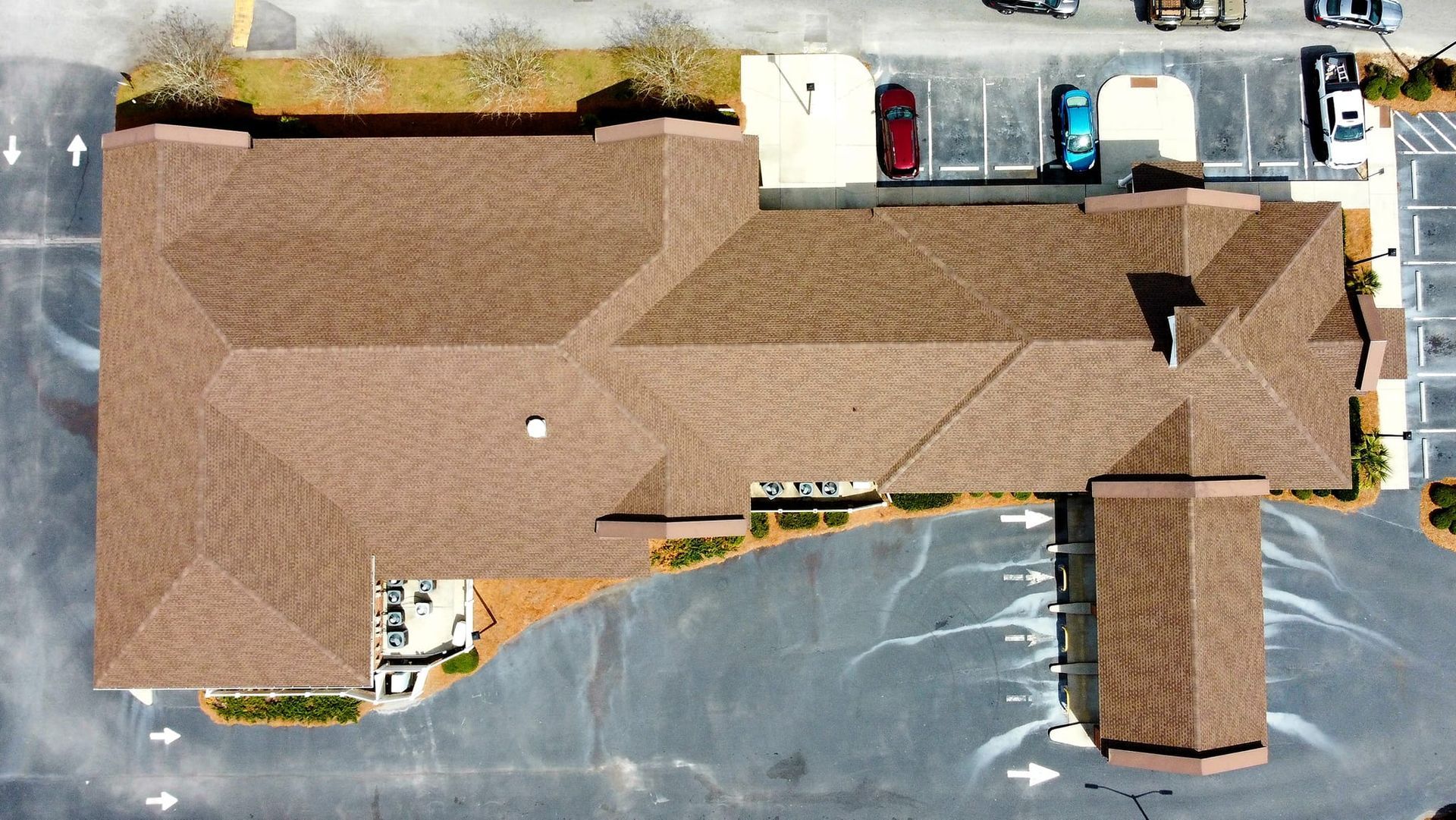 Overhead view of a brown-roofed building with parking lot and cars.