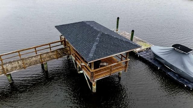 Wooden dock with covered gazebo and boat on calm water.