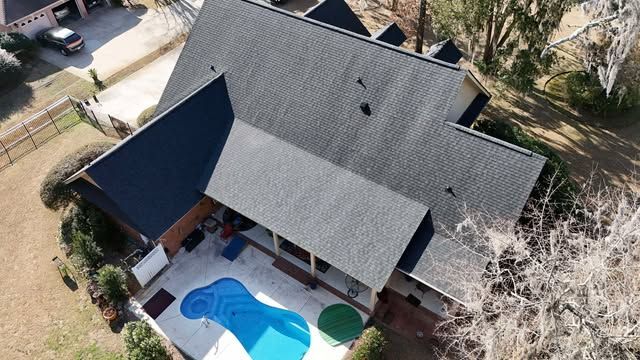 Aerial view of a house with a dark gray roof, pool, and surrounding yard.