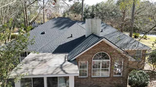 A two-story brick house with a dark gray roof. The house is surrounded by trees.