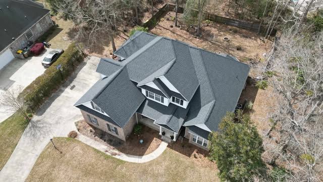 Aerial view of a gray-roofed house with a driveway surrounded by trees and a lawn.