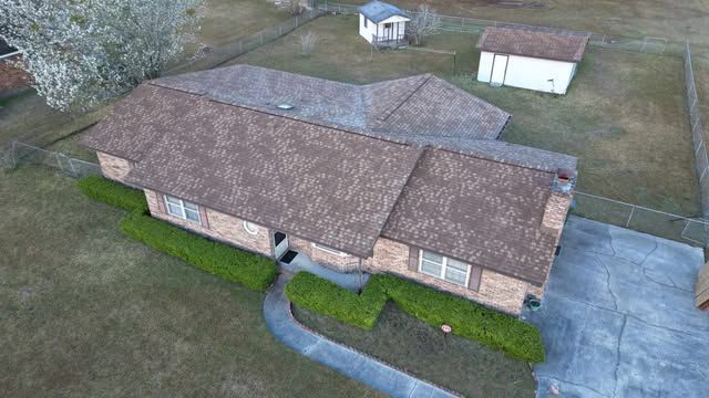 Aerial view of a brown brick house with a brown roof and green bushes in front.