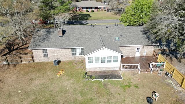 Aerial view of a brick house with a dark gray roof, deck, and large backyard with a yellow fence.
