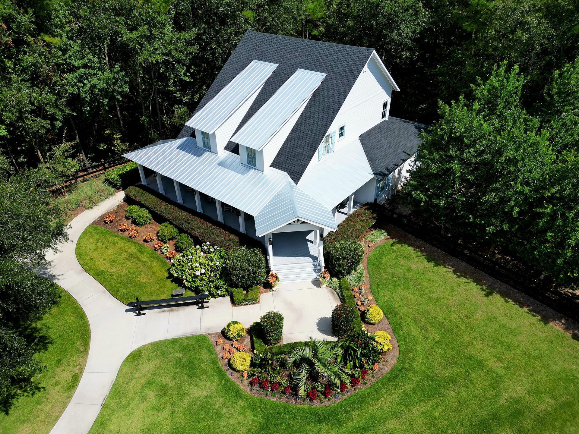 Aerial view of a white house with a dark roof surrounded by green trees.