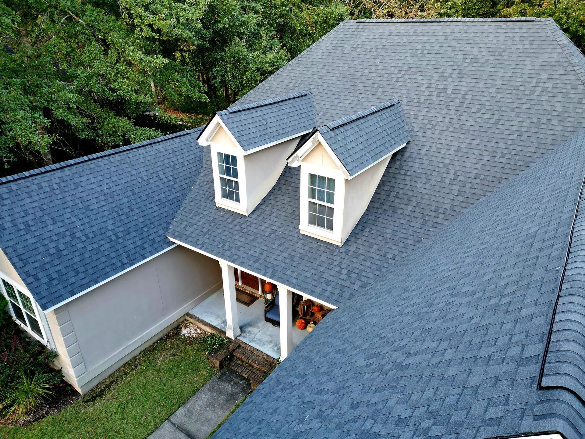Aerial view of a house with a dark gray shingle roof and two dormers with windows.