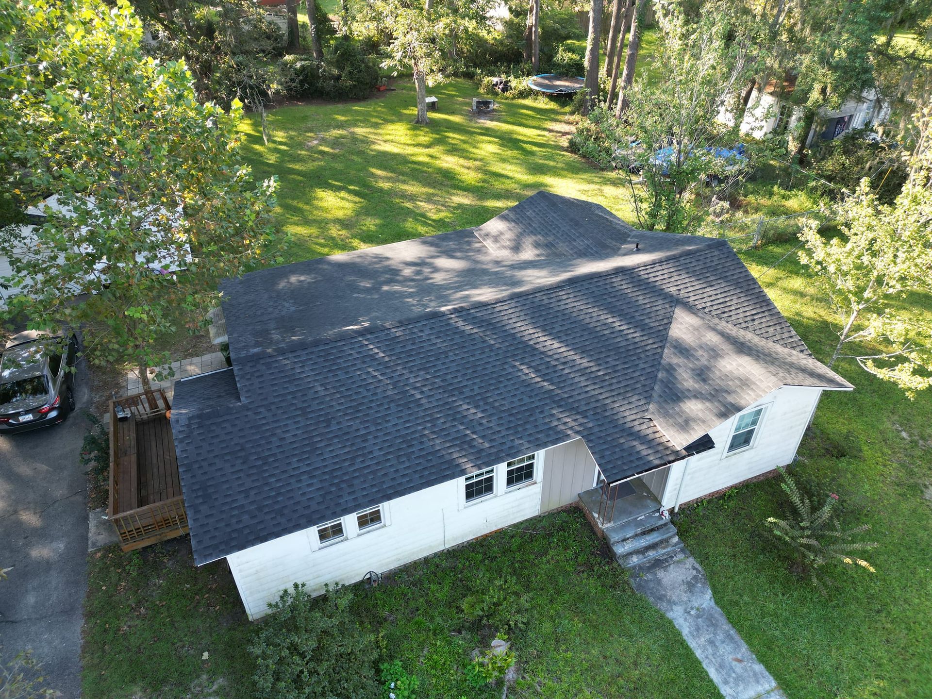 Overhead view of a white house with a dark roof surrounded by green grass and trees.