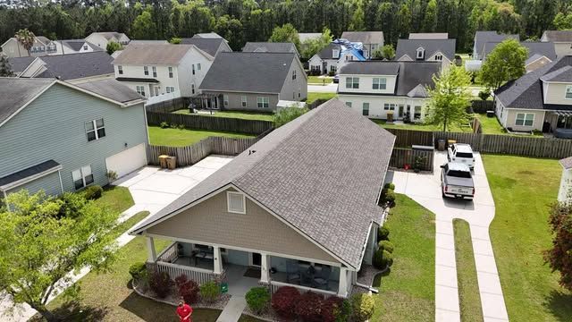 Aerial view of suburban houses with manicured lawns and cars parked in driveways on a sunny day.
