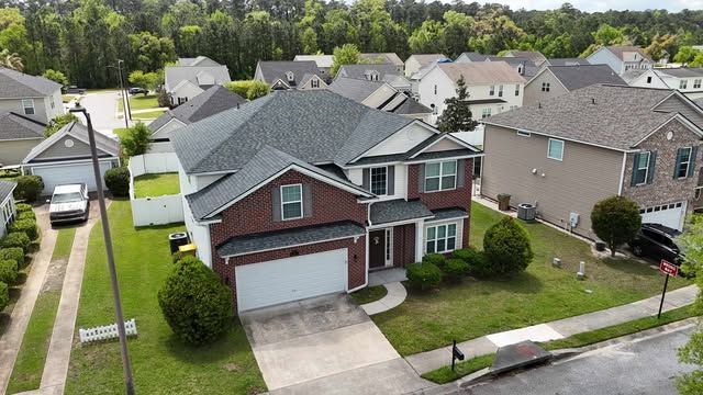 Two-story brick-front house with a gray roof and attached garage in a suburban neighborhood.