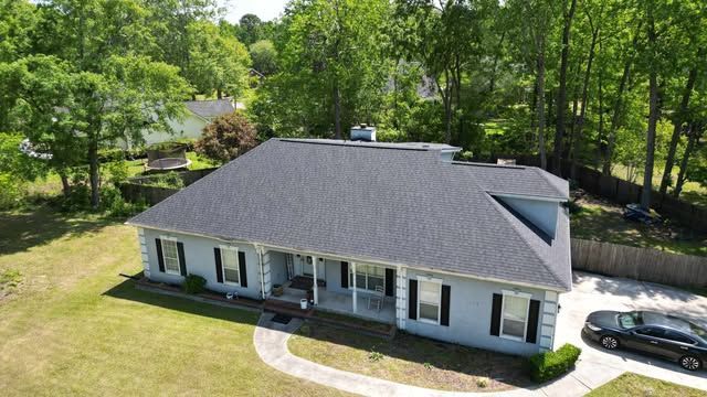 Aerial view of a house with a gray roof surrounded by green trees and a white car in the driveway.