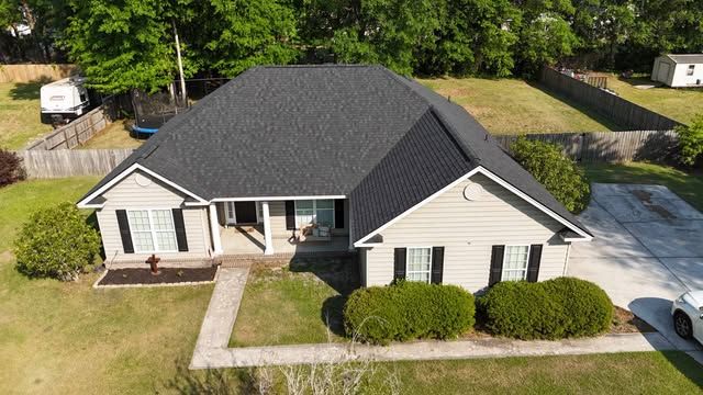 Overhead view of a house with a brown shingled roof, set on green grass.