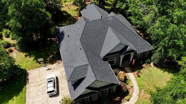 Aerial view of a dark roof house with a rectangular pool and green lawn.