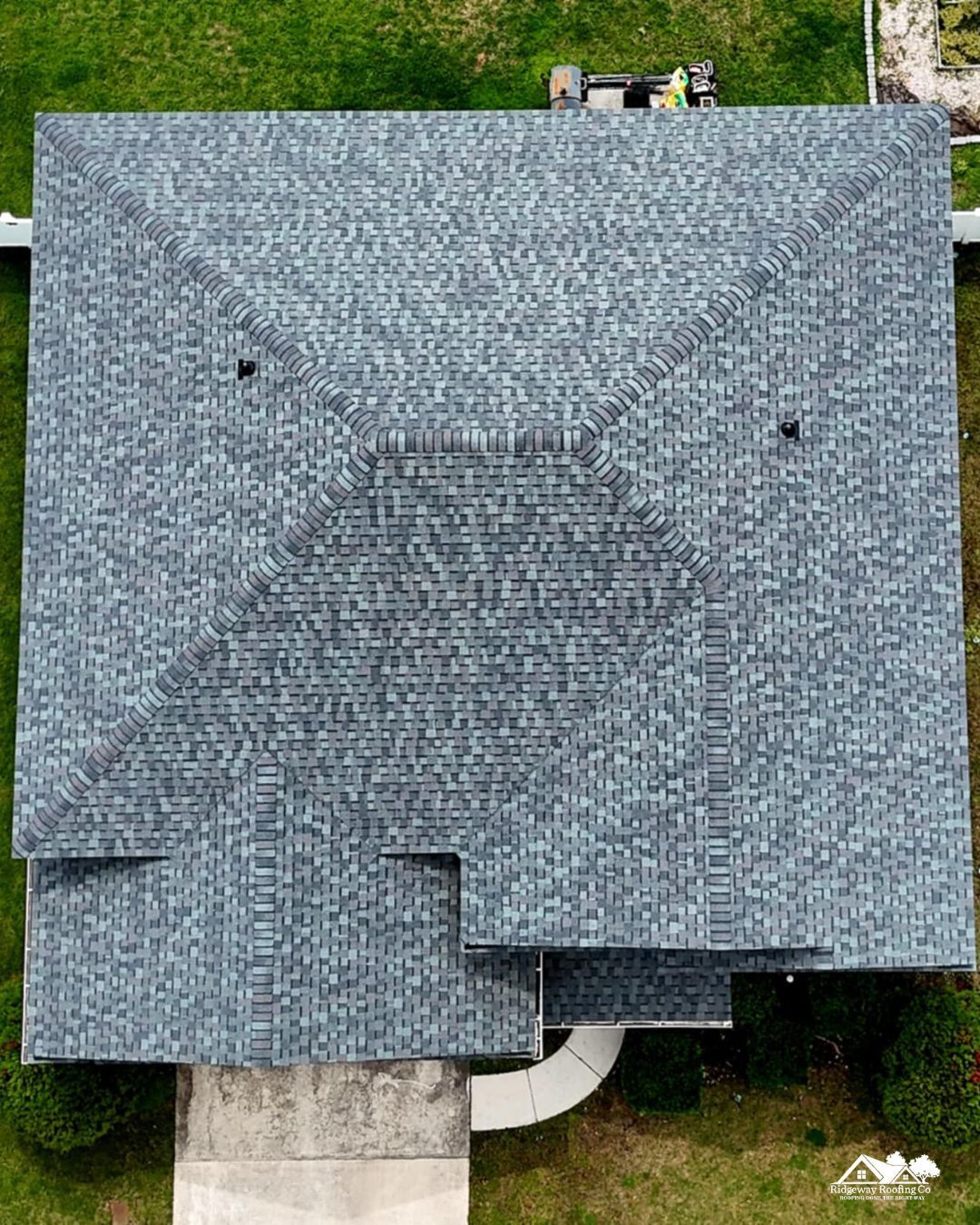 Overhead view of a house with a gray shingle roof, surrounded by green grass.